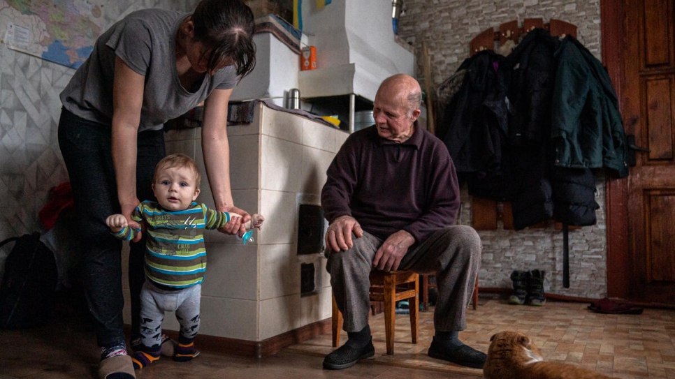 Svitlana helps Matvii take a few steps while her grandfather, Ivan, looks on.