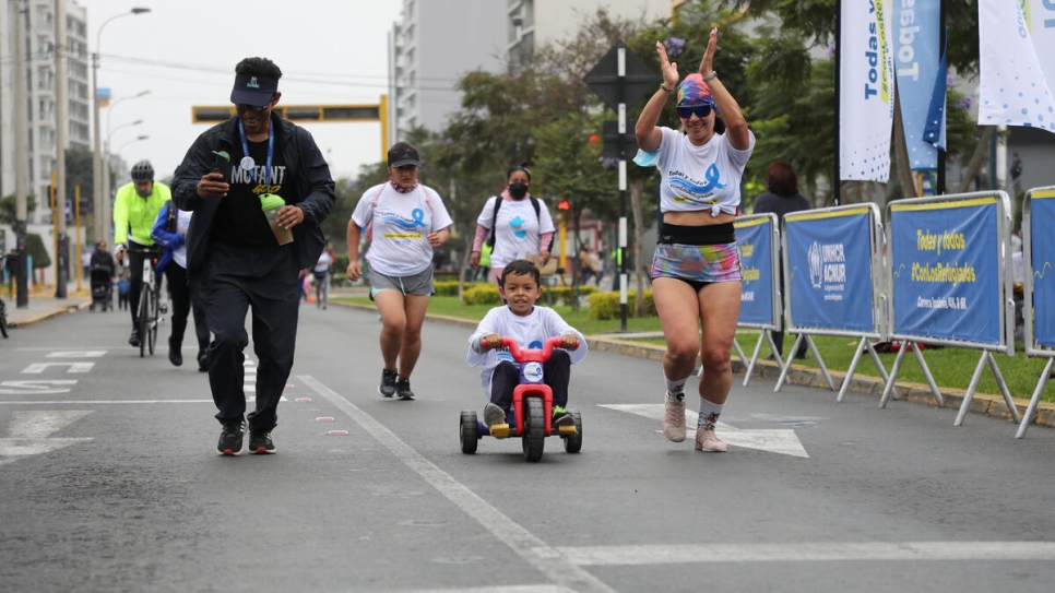 A young boy riding a tricycle accompanies his mother across the finish line.
