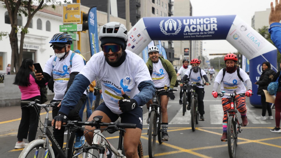 A group of cyclists reach the finish line wearing t-shirts with World Refugee Day messages.