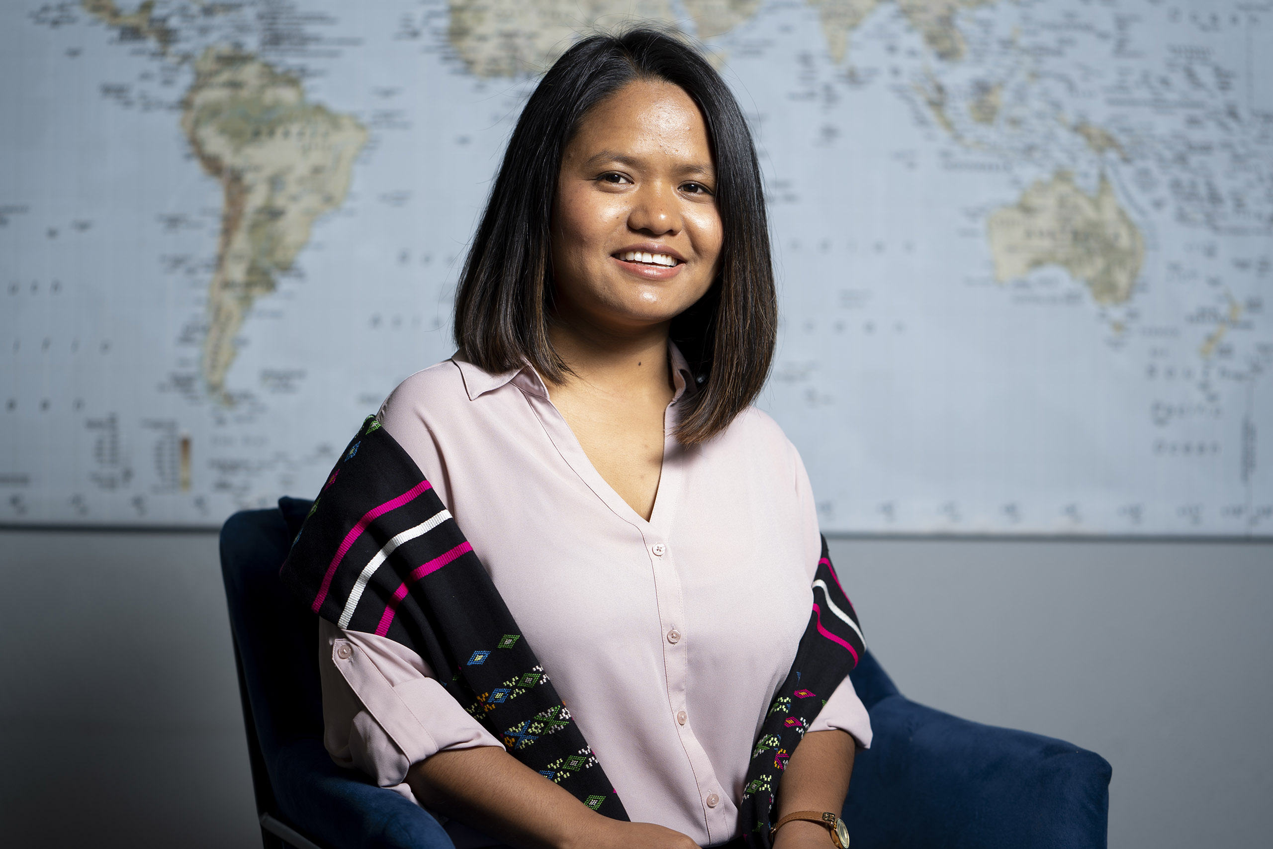 Burmese-American woman in pink blouse seated in front of a world map.