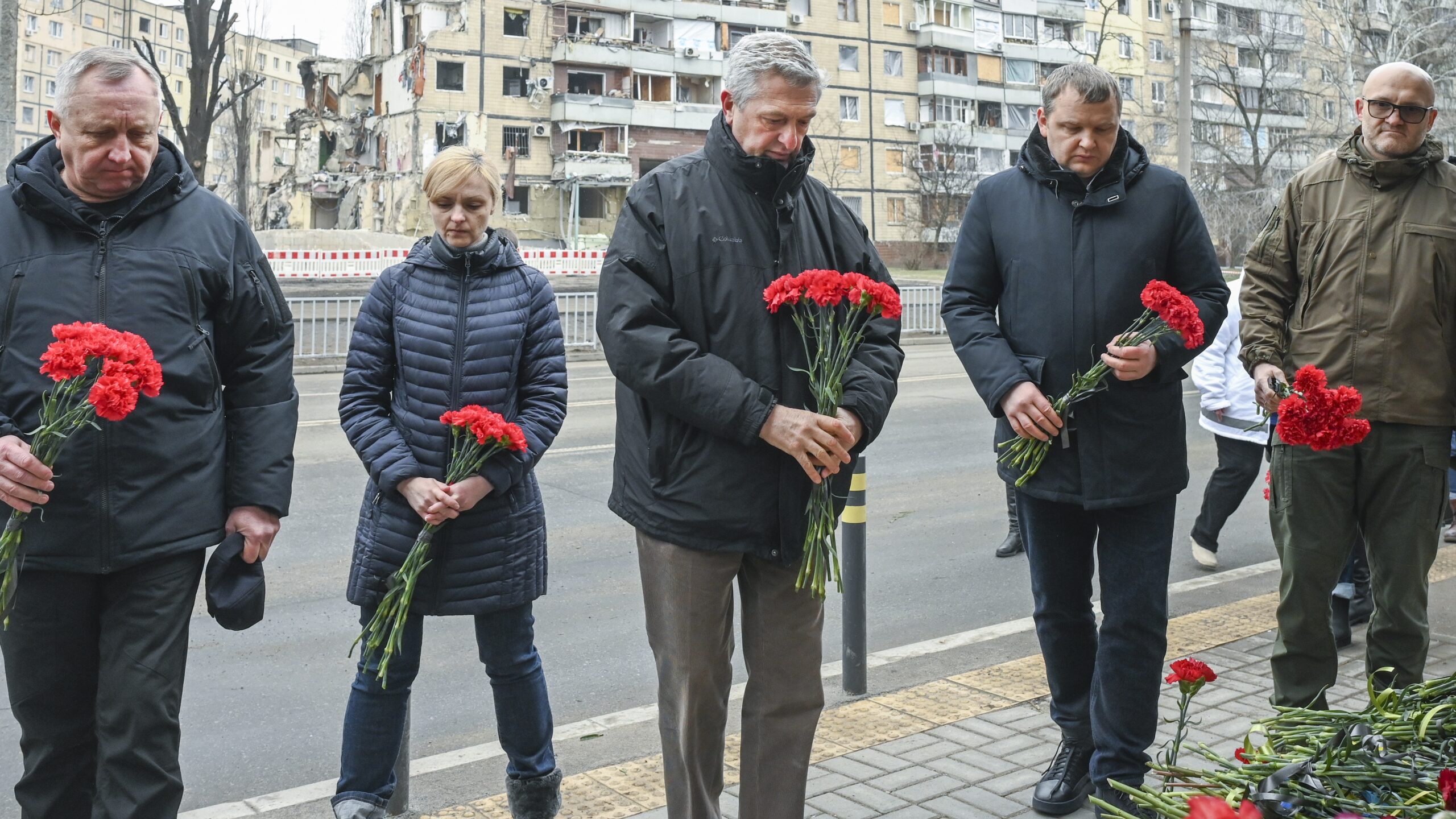 Le Haut Commissaire Filippo Grandi (au centre), aux côtés de représentants des autorités locales, dépose des fleurs devant un immeuble résidentiel détruit par un tir de missile le 14 janvier 2023, dans la ville de Dnipro, en Ukraine. © HCR/Colin Delfosse