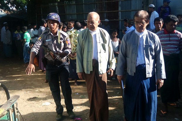 Members of Myanmar's advisory commission on Rakhine State, Win Mra (C) and Khin Maung Lay (R) are escorted by an armed policeman during a visit to a Rohingya camp in Sittwe, capital of Rakhine State, Nov. 16, 2016.