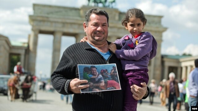 Syrian refugee Laith Majid Al-Amirij and his 7-year-old daughter Noor pose in front of the Brandenburg Gate in Berlin while holding a famous photo showing them during their crossing to the Greek island of Kos.