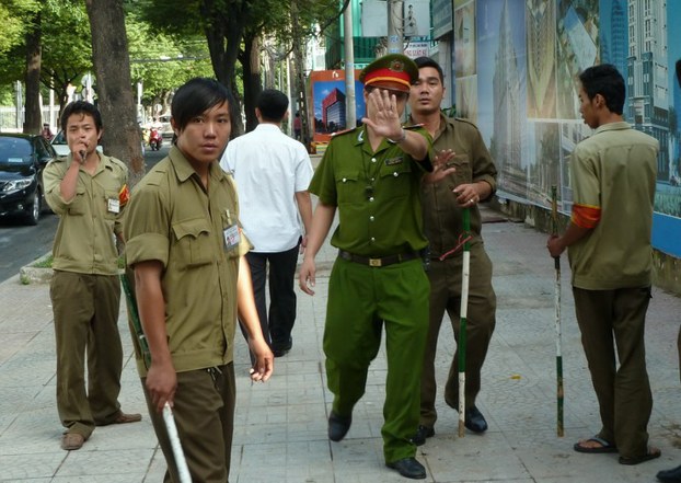 A policeman, flanked by local militia members, guards the outside of the Ho Chi Minh City People's Court, Aug. 10, 2011.