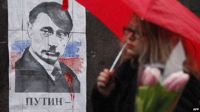 Not the first time: A woman walks in front of a poster in Kyiv on March 3 depicting Russian President Vladimir Putin as Adolf Hitler and signed 'Hands off Ukraine.'