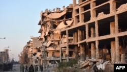 Syrian pro-government forces walk past destroyed buildings in Aleppo's Bustan al-Basha neighborhood on November 28