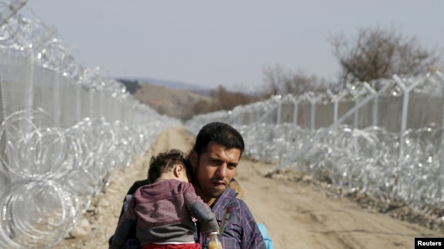 A migrant from Afghanistan holding a child walks next to a border fence at the Macedonian-Greek border in Gevgelija.