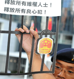 A protester holds a paper-made prison door in front of a policeman (R) standing guard during Chinese Vice Premier Li Keqiang's visit to Hong Kong, Aug. 18, 2011.