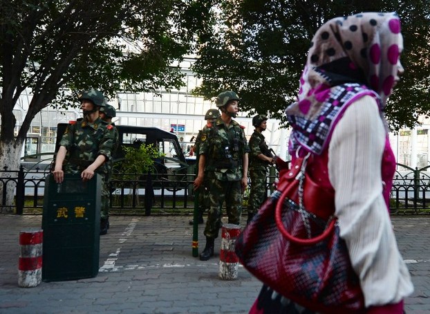 A Uyghur woman walks past paramilitary police on a street in the Xinjiang capital Urumqi, June 30, 2013.