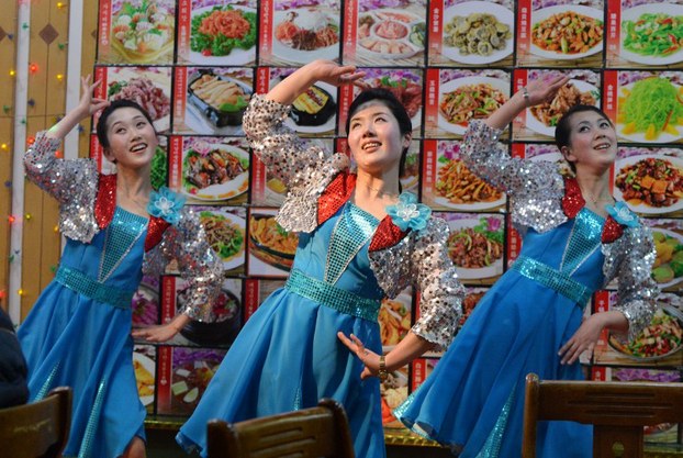 North Korean waitresses perform in front of a large menu at a North Korean-owned restaurant in the Chinese border town of Dandong, Feb. 11, 2013.