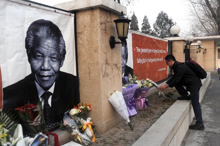 A man lays flowers in front of a portrait of Nelson Mandela outside the South African Embassy in Beijing, Dec. 6, 2013.
