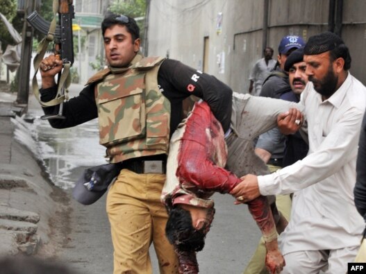 A Pakistani policeman carries the bloodied body of a worshiper at one of two mosques stormed by gunmen in Lahore.