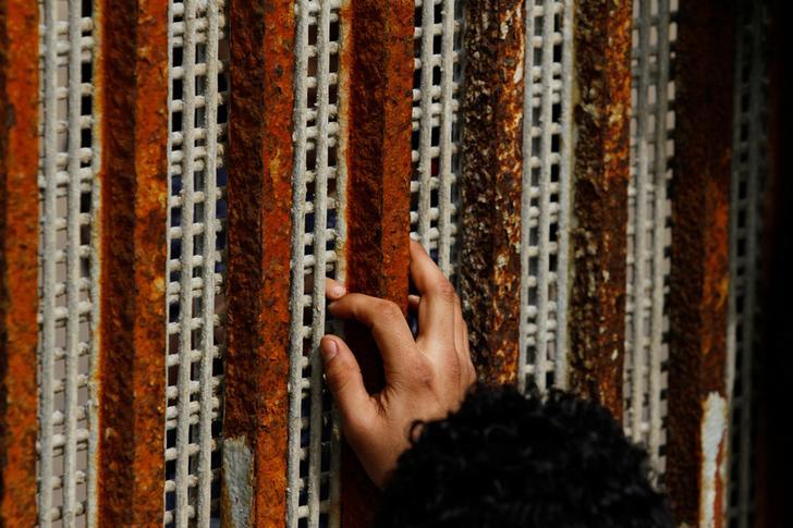 A man, who was deported from the U.S. seven months ago, touches the fingertips of his nephew across a fence separating Mexico and US, as photographed from Tijuana, Mexico, March 4, 2017. 