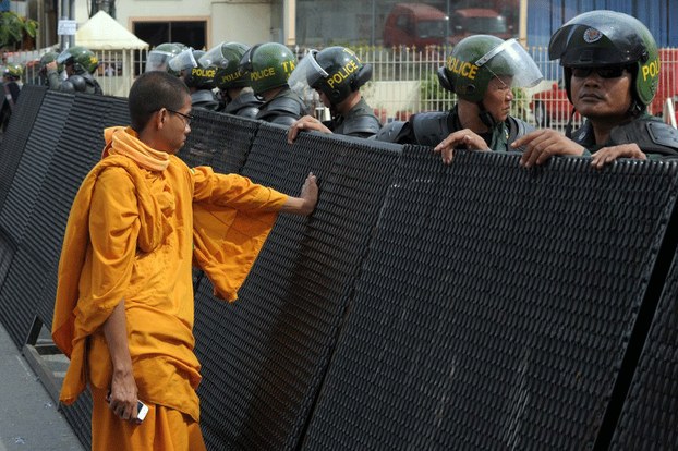 A Cambodian Buddhist monk (L) stands next to a barricade in front of police near the Phnom Penh Municipal court, May 6, 2014.