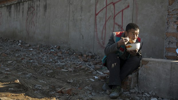 A worker eats his meal near a wall marked for demolition in Beijing, Dec. 11, 2015.