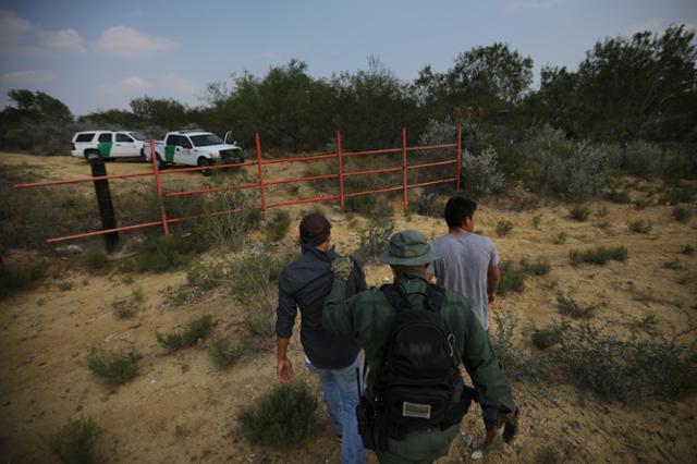 A U.S. border patrol agent escorts men being detained after entering the United Statesby crossing the Rio Grande river from Mexico, in Roma, Texas, U.S., May 11, 2017. 