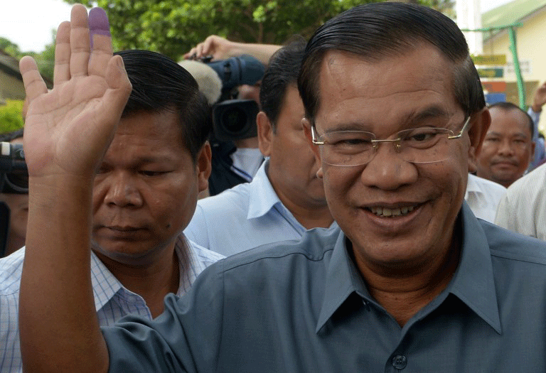 Prime Minister Hun Sen (R) waves after casting his vote in elections in Kandal province, July 28, 2013