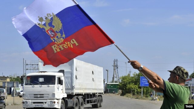 A local resident holds a Russian national flag as trucks, part of a Russian humanitarian convoy, cross the Ukrainian border at the Izvarino custom control checkpoint.