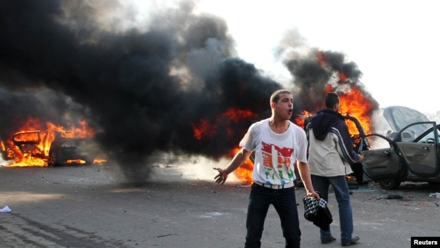 Antigovernment protester shouts slogans in front of burning cars during clashes with pro-government supporters in Alexandria on December 14.