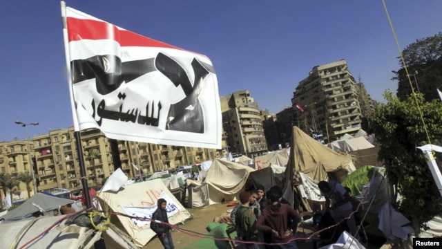 Antigovernment protesters sit outside their tents below a flag that says 'No to the constitution,' on Tahrir Square in Cairo on December 10.