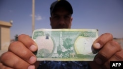 An Iraqi policeman holds a 10,000-Iraqi dinar note bearing an image of Mosul's leaning minaret, now destroyed.