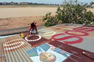 A Cambodian girl paints 'SOS' under a portrait of US President Barack Obama on the roof of a building next to the Phnom Penh International Airport, Nov. 14, 2012.