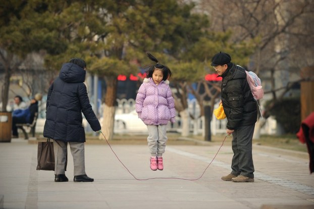 A girl plays jump rope with her family by a road in Beijing, Dec. 7, 2012.