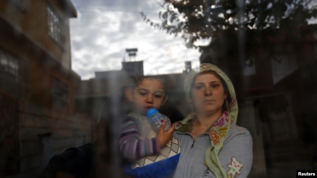 A Syrian refugee woman holds her son as she stands at the window of their friend's house at the Syrian-Turkish border town of Ceylanpinar in Syria.