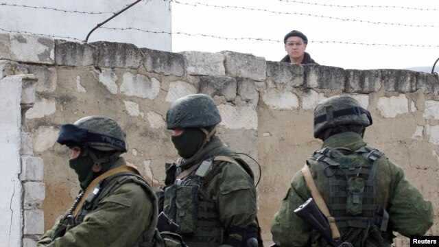 A Ukrainian serviceman peers over a wall at uniformed men, believed to be Russian servicemen, standing guard at a Ukrainian military base in the village of Perevalnoye, outside the Crimean capital, Simferopol, on March 6.