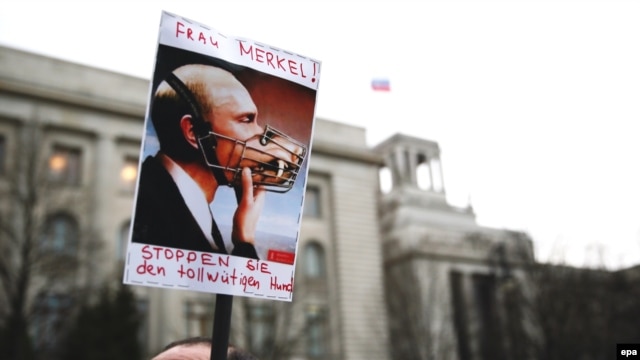 A Ukrainian demonstrates with a poster depicting Russian President Vladimir Putin with a muzzle and text calling on German Chancellor Angela Merkel to 'stop the mad dog' in front of the Russian embassy in Berlin on March 17.
