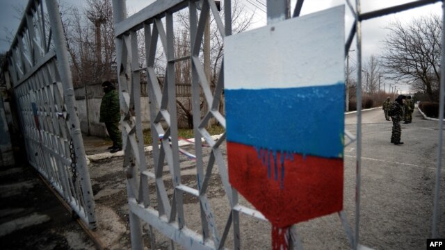 Members of the new pro-Russian forces dubbed the 'military forces of the autonomous republic of Crimea' stand at a gate, adorned with a Russian flag, of Simferopol's republican military enlistment complex on March 10.