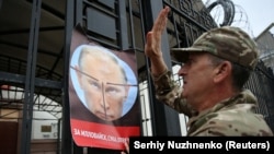 A demonstrator puts up a poster depicting Russian President Vladimir Putin during a rally to commemorate the fourth anniversary of the battle in the eastern city of Ilovaysk, in front of the Russian Embassy in Kyiv, on August 29.