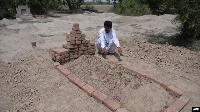 The husband of Farzana Parveen, who was stoned to death by her father and other family members, sits beside her grave.