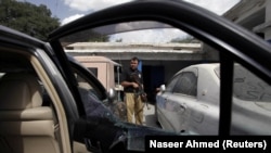 A police officer is seen next to the damaged car of Malik Naveed, a Pakistani regional political party leader, who was killed by unidentified gunmen in Quetta on July 6.