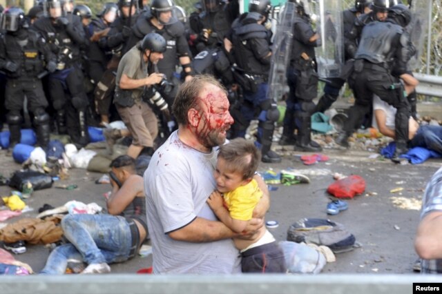 An injured migrant carries a child during clashes with Hungarian riot police at the border crossing with Serbia in Roszke on September 16.