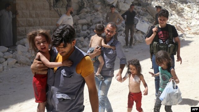 Syrian men carry injured children amid the rubble of destroyed buildings following reported air strikes on the rebel-held neighborhood of Al-Mashhad in the northern city of Aleppo on July 25.
