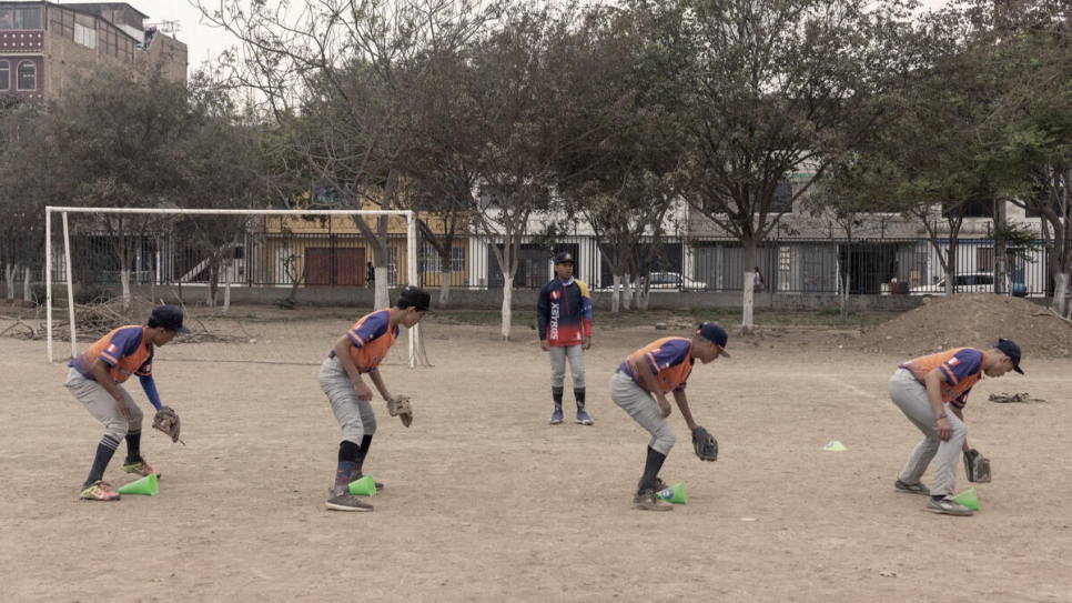 A line of players wearing mitts run fielding drills