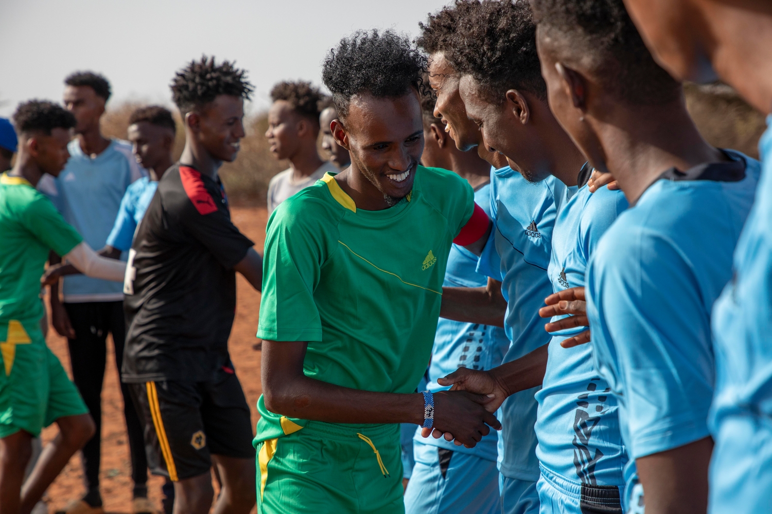 Football players in green and blue shirts greet each other.